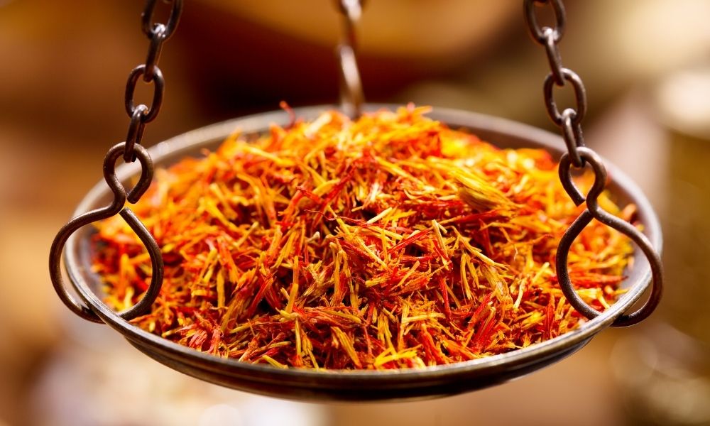 Ein dunkler metalllöffel mit leuchtend orange und roten safranfäden für kunkumadi gesichtsöl bei trockener haut im mana shop