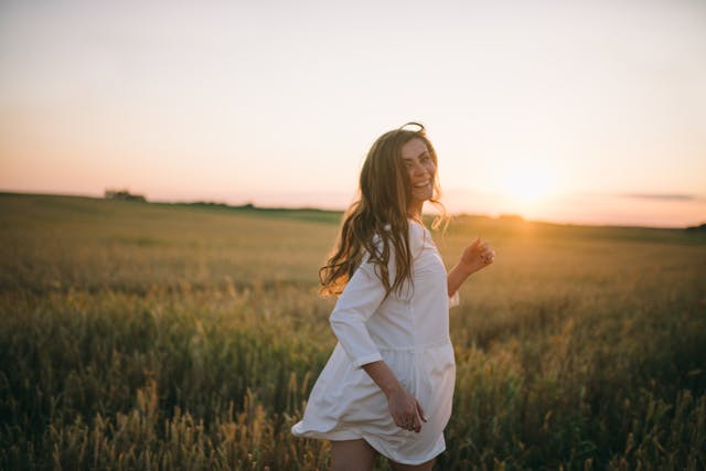 Eine frau in einem fließenden weißen kleid steht in goldenen weizenfeldern bei sonnenuntergang natürliche alternativen für nachhaltige energie im mana shop