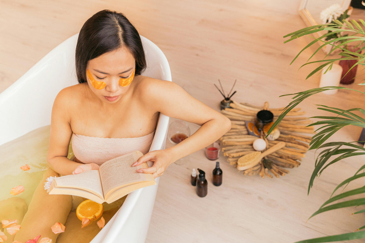 Frau mit dunklen haaren und orangen augenmasken im badezimmer mit blütenblättern zum ayurveda frühlings-detox sanft reinigen