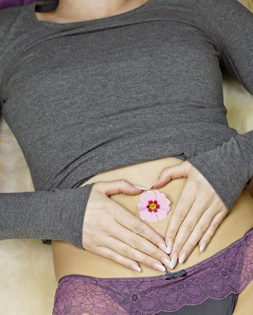 Eine zarte rosa blume mit gelbem mittelpunkt zwischen händen in herzform über dem bauch ayurveda verdauungstipps