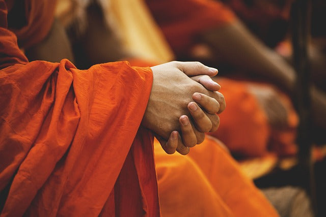 Eine paar hände in einer meditativen pose mit leuchtend orangefarbenen monastischen roben spirituelle energetische produkte