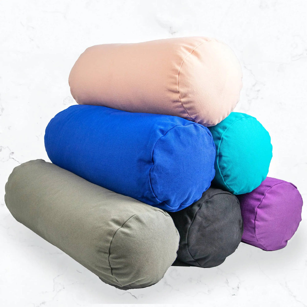 Ein stapel weicher yoga bolsters in pastellpink, royalblau, teal, olive, anthrazit und lila für yin yoga im mana shop kaufen