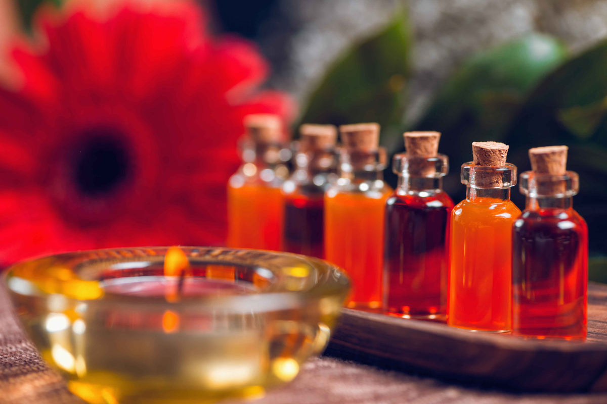 Kleine Glasfläschchen mit ätherischen Ölen und brennende Kerze vor roter Blume.