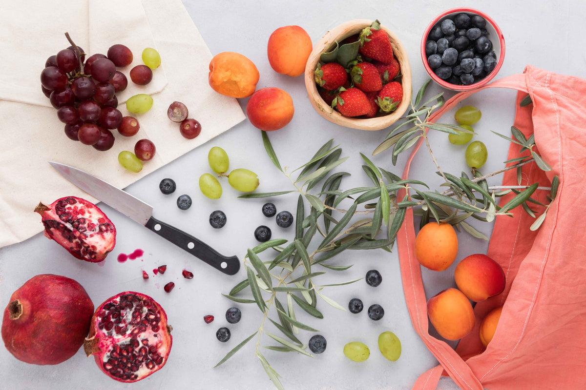 Frisches Bio-Obst wie Granatäpfel, Weintrauben, Erdbeeren und Aprikosen auf hellem Untergrund.