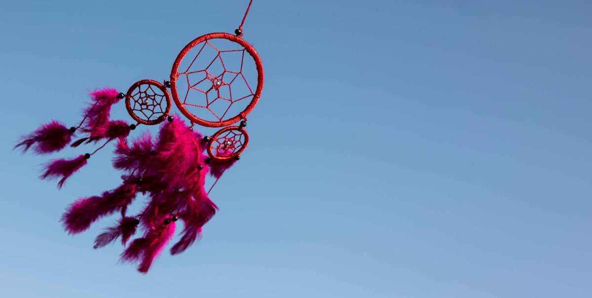 Roter Traumfänger mit Federn vor blauem Himmel