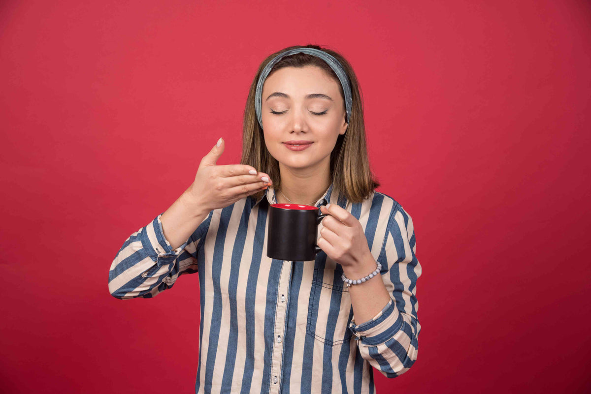 Junge Frau mit geschlossenen Augen genießt einen heißen Tee aus einer schwarzen Tasse.