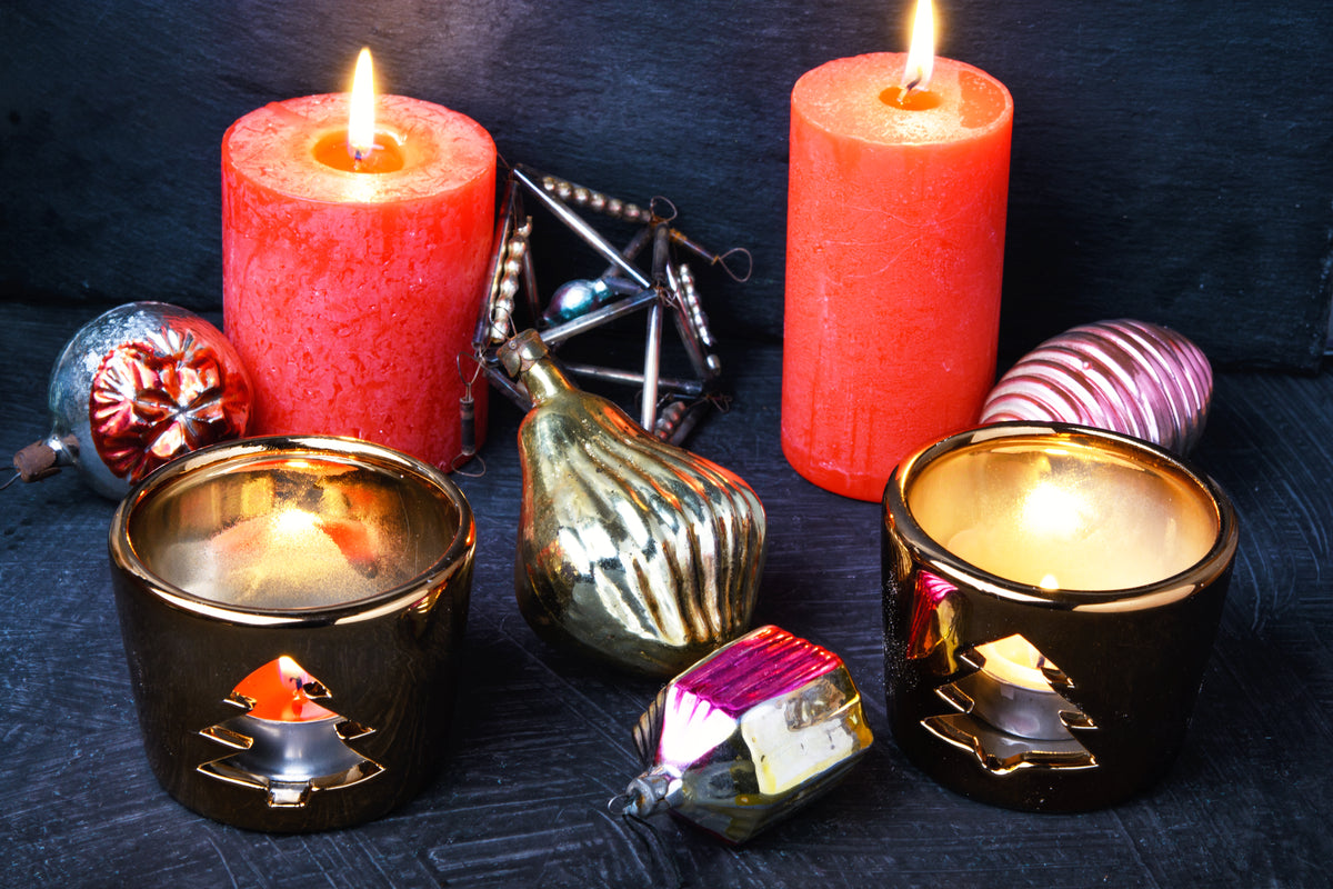 Rote Kerzen und goldene Teelichthalter mit Weihnachtsdekoration auf dunklem Untergrund.
