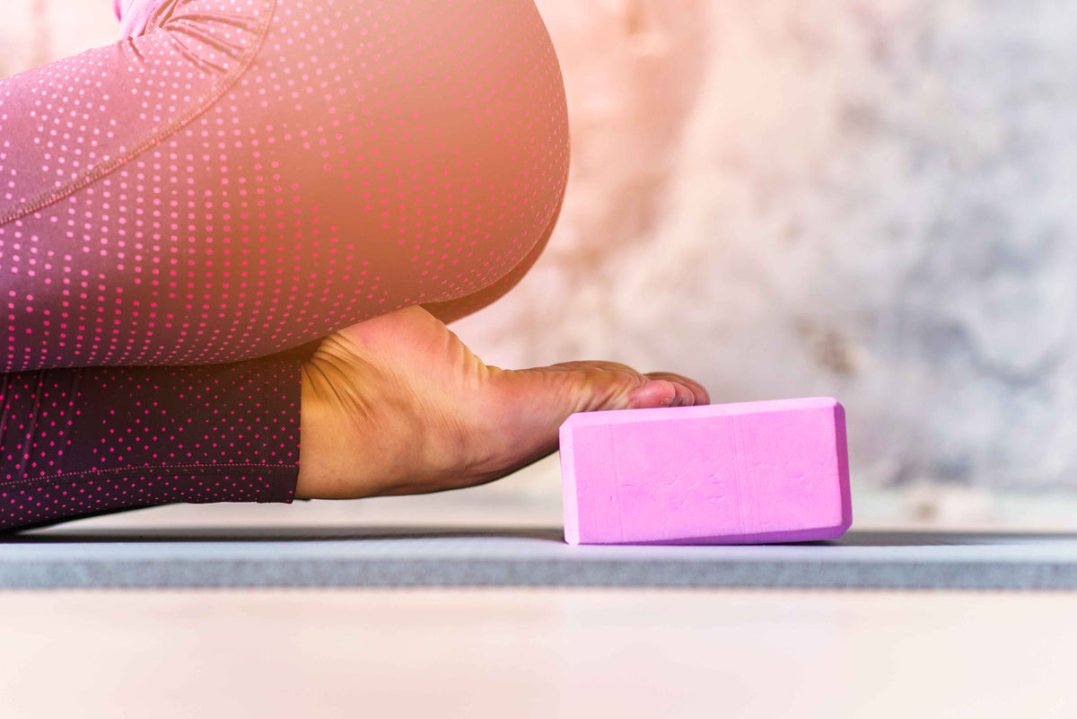 Yoga-Übung mit rosa Yoga-Block und Person in Sportbekleidung auf einer Matte.