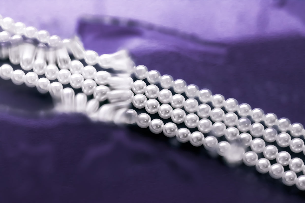 Elegante weiße Perlenkette auf violettem Stoffhintergrund.
