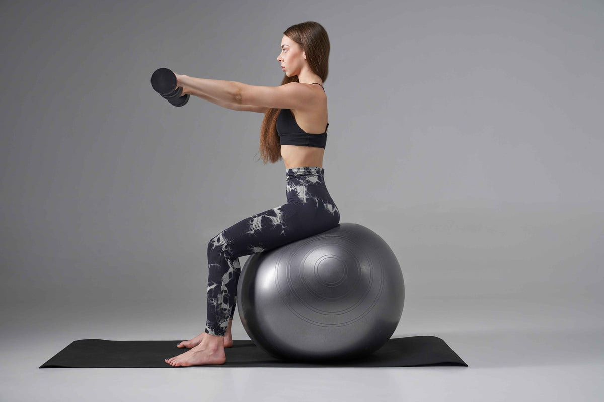 Frau macht Fitnessübungen mit Hantel auf einem Gymnastikball für Yoga und Training.
