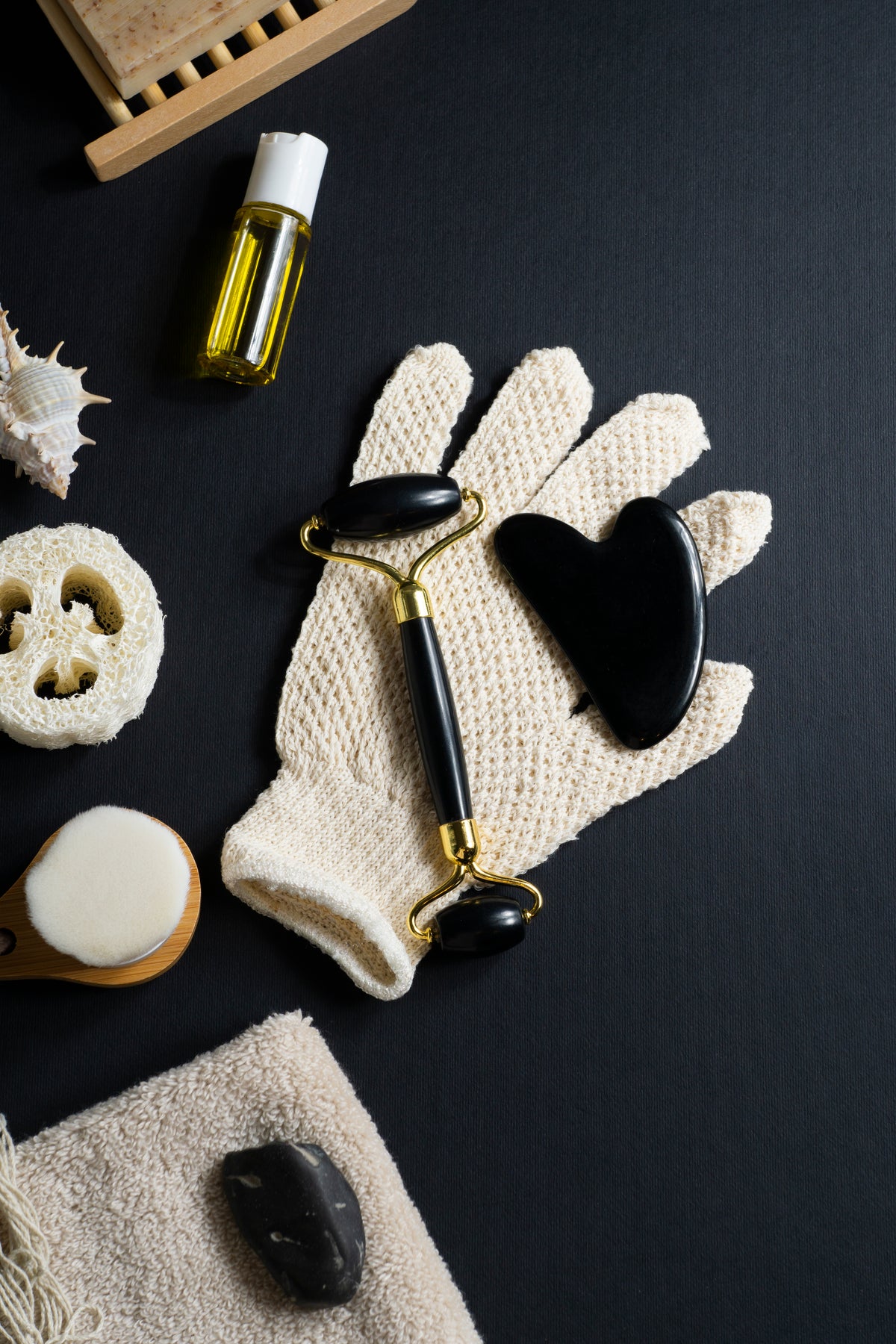 Wellness-Set mit Jade-Roller, Gua Sha Stein, Peelinghandschuh und Naturkosmetik auf schwarzem Grund.