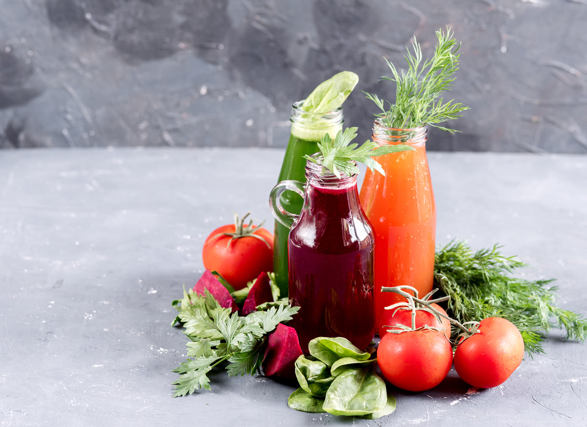 Frische Bio-Gemüsesäfte in Glasflaschen mit Tomaten, Roter Bete und frischen Kräutern.