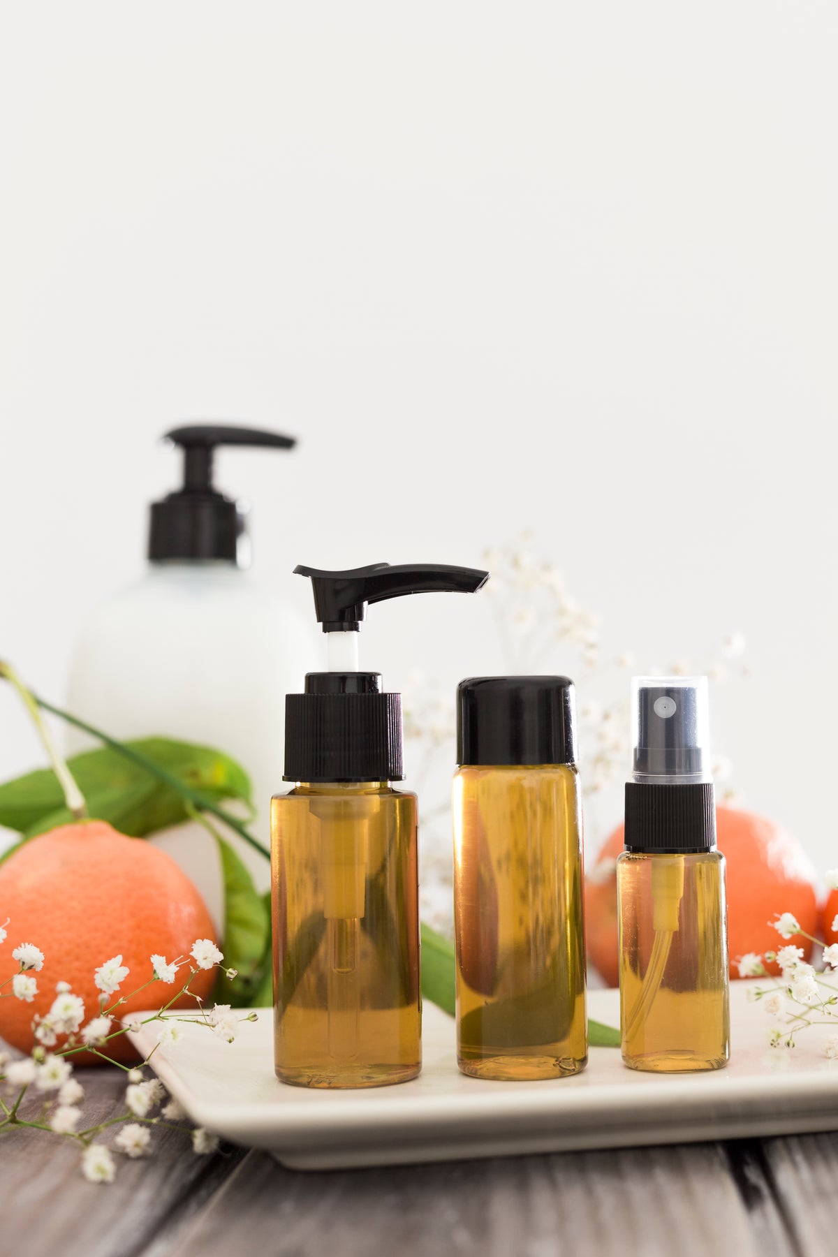 Bio-Kosmetik Flaschen in Braunglas mit Sprühpumpen auf einem Tablett mit Blumen und Früchten