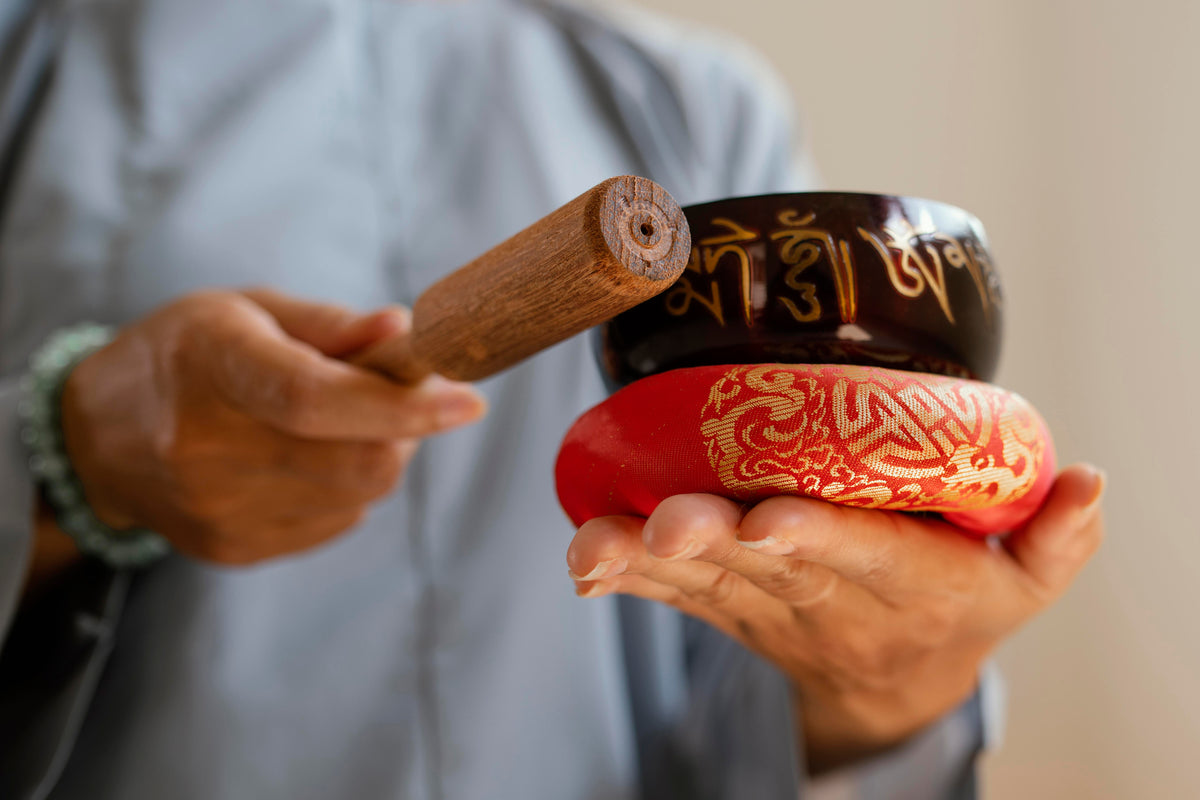 Person spielt eine tibetische Klangschale mit Holzschlägel für Meditation und Yoga.