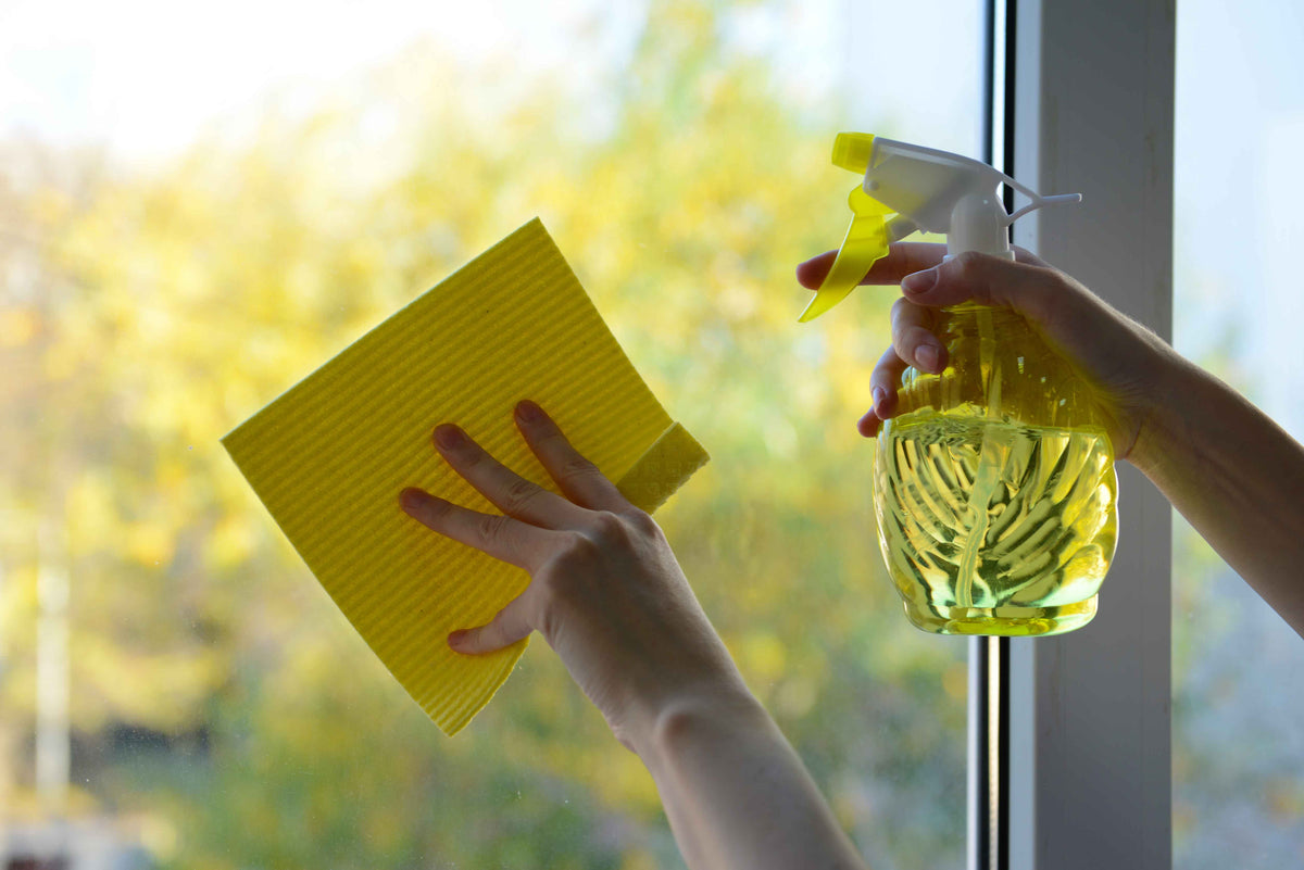 Reinigen einer Fensterscheibe mit gelbem Reinigungstuch und Sprühflasche