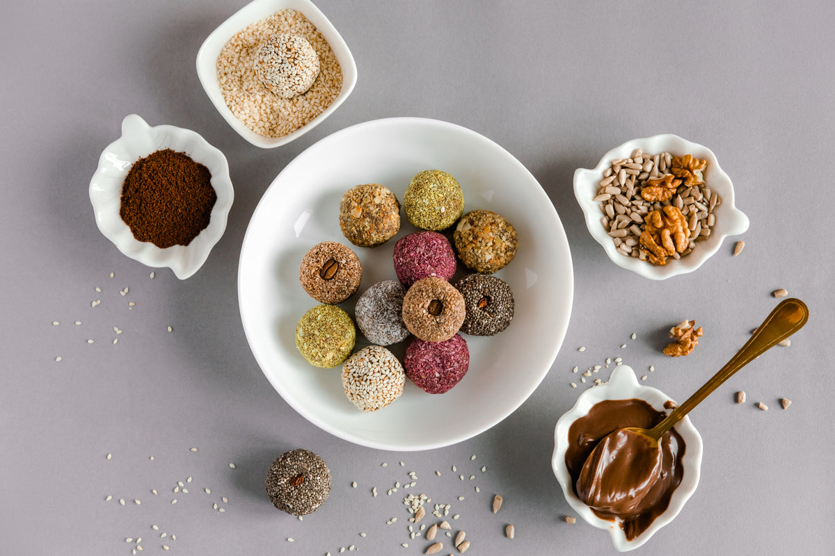 Gesunde Energy Balls mit verschiedenen Toppings wie Sesam, Chia und Nüssen auf einem weißen Teller.