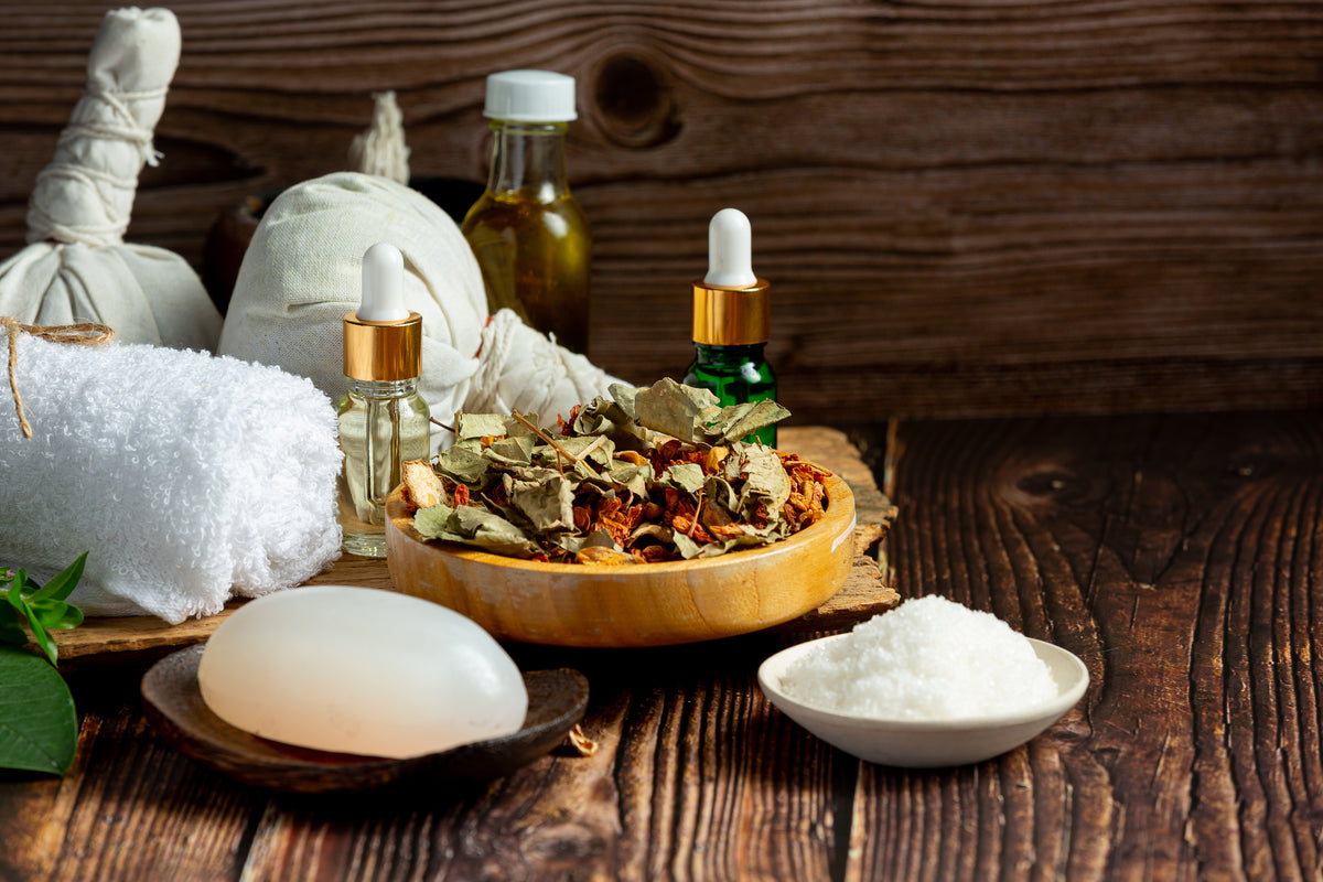 Bio-Kosmetik Set mit ätherischen Ölen, Kräutern, Seife und Massage-Säckchen auf Holz.