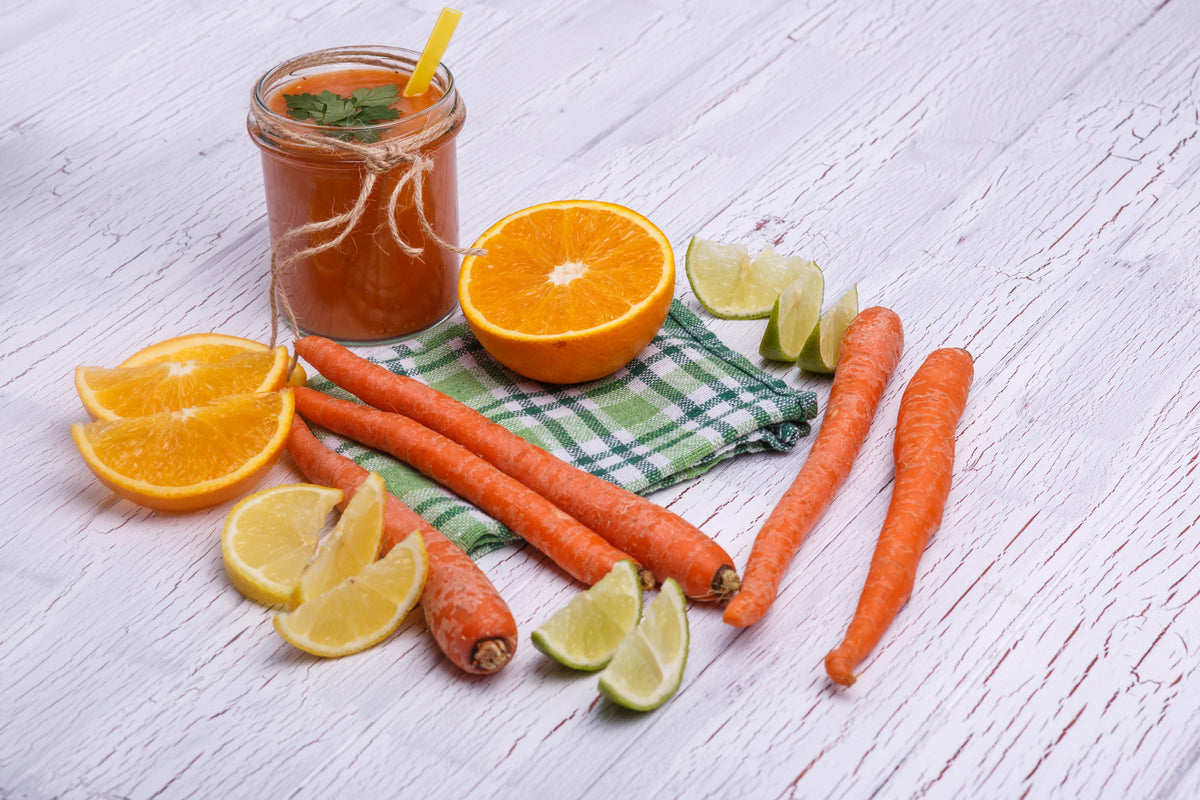 Frischer Karotten-Orangen-Smoothie im Glas mit Zitrusfrüchten und Bio-Karotten auf Holztisch.