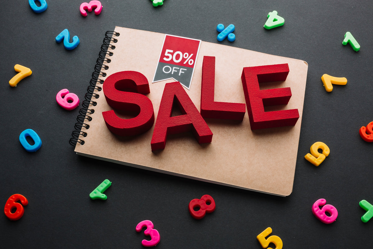 Sale-Angebot mit 50% Rabatt auf einem Notizblock und bunten Zahlen auf schwarzem Hintergrund.