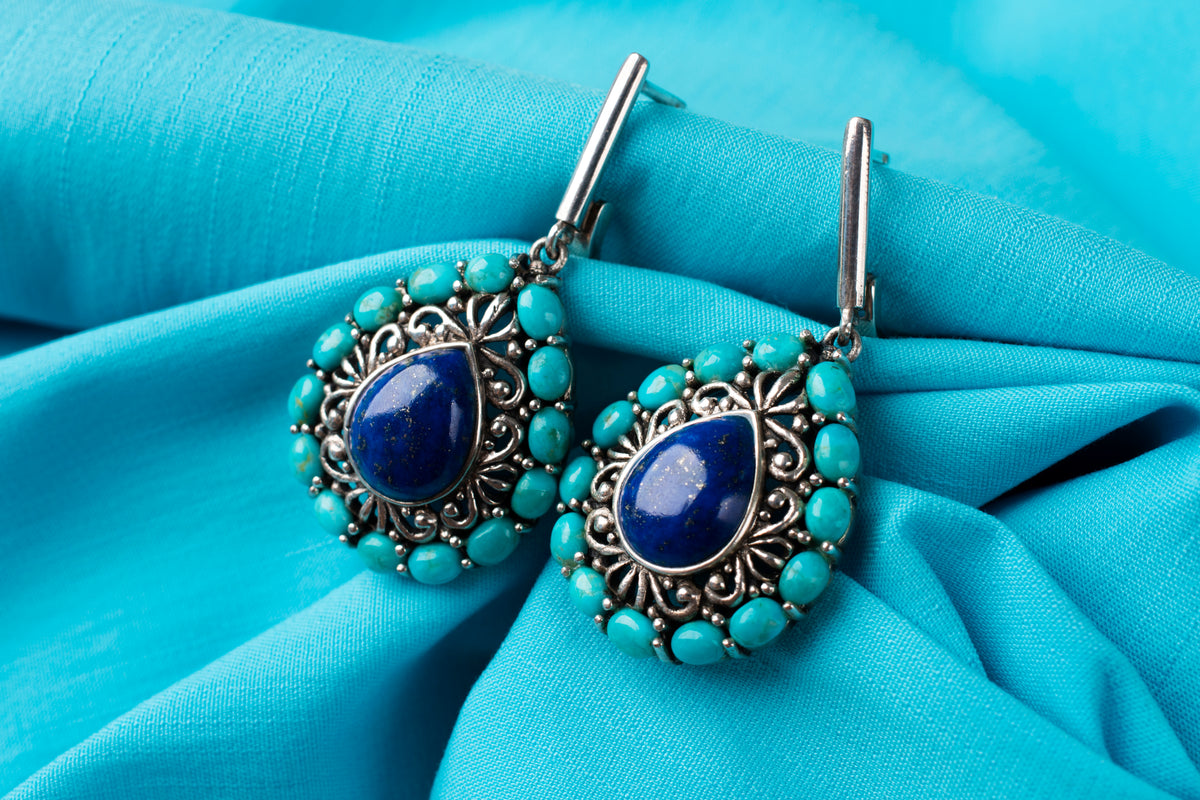 Elegante Ohrringe mit blauem Lapis Lazuli und türkisfarbenen Steinen auf blauem Stoff.