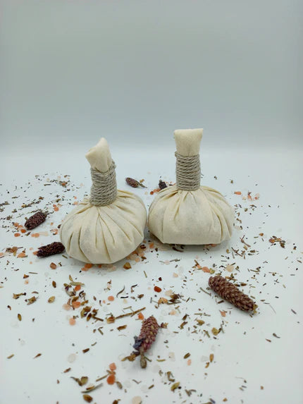 Zwei handgemachte Kräuterballen aus Bio-Baumwolle auf getrockneten Kräutern und Blüten.