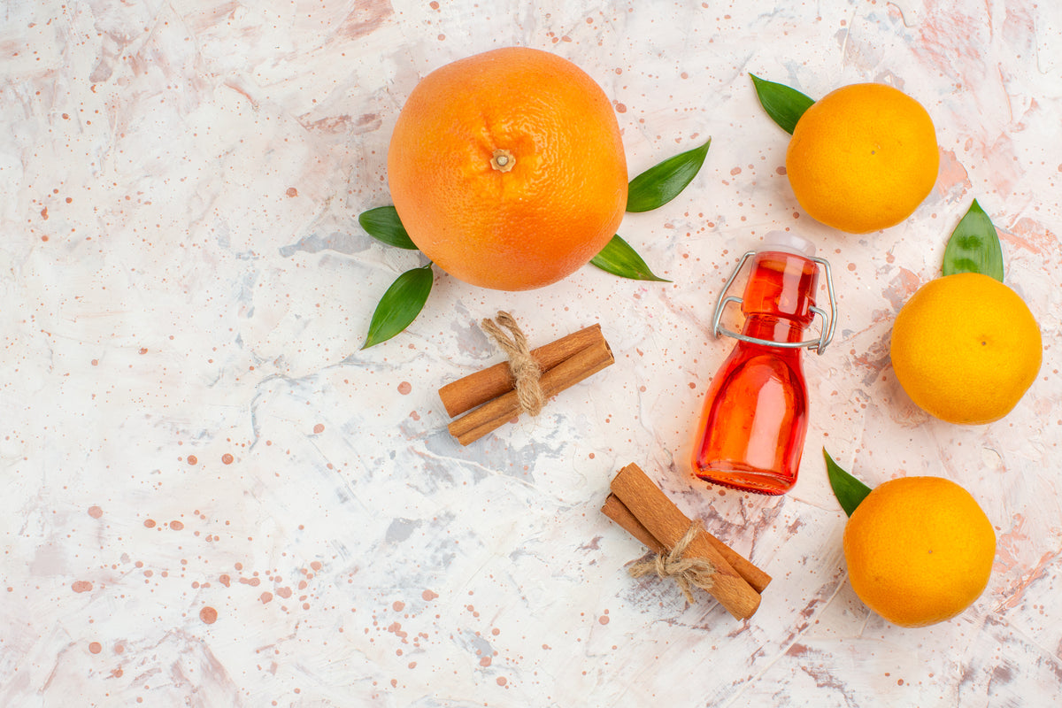 Frische Orangen, Zimtstangen und ein Fläschchen rotes Öl auf hellem Hintergrund.