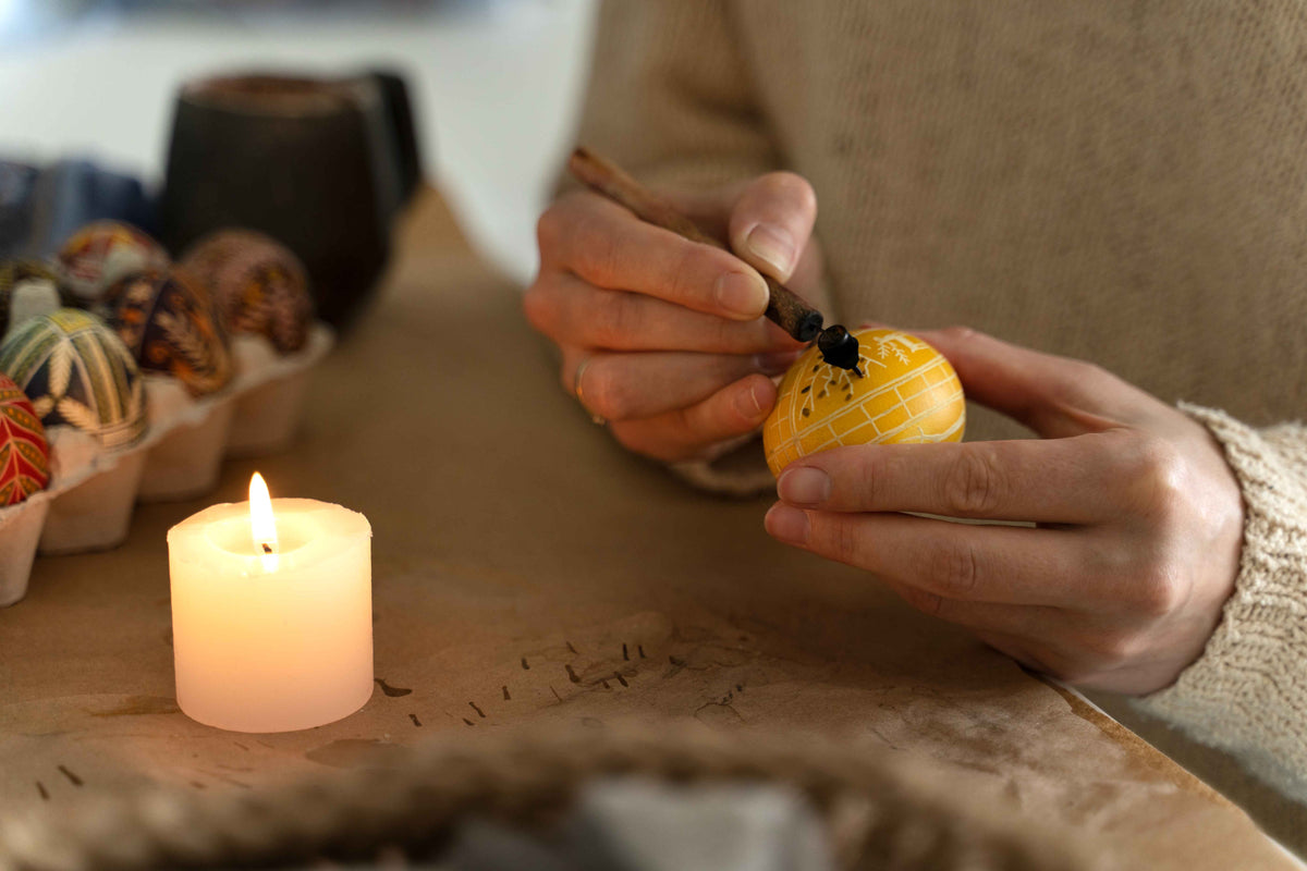 Handbemalte gelbe Osterei-Dekoration mit traditionellen Mustern und brennender Kerze.