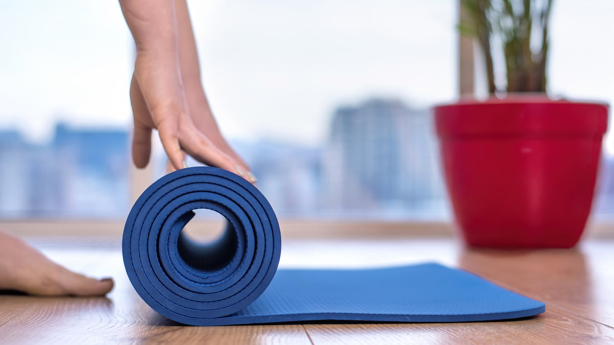 Eine Person rollt eine blaue Yogamatte auf einem Holzboden aus.