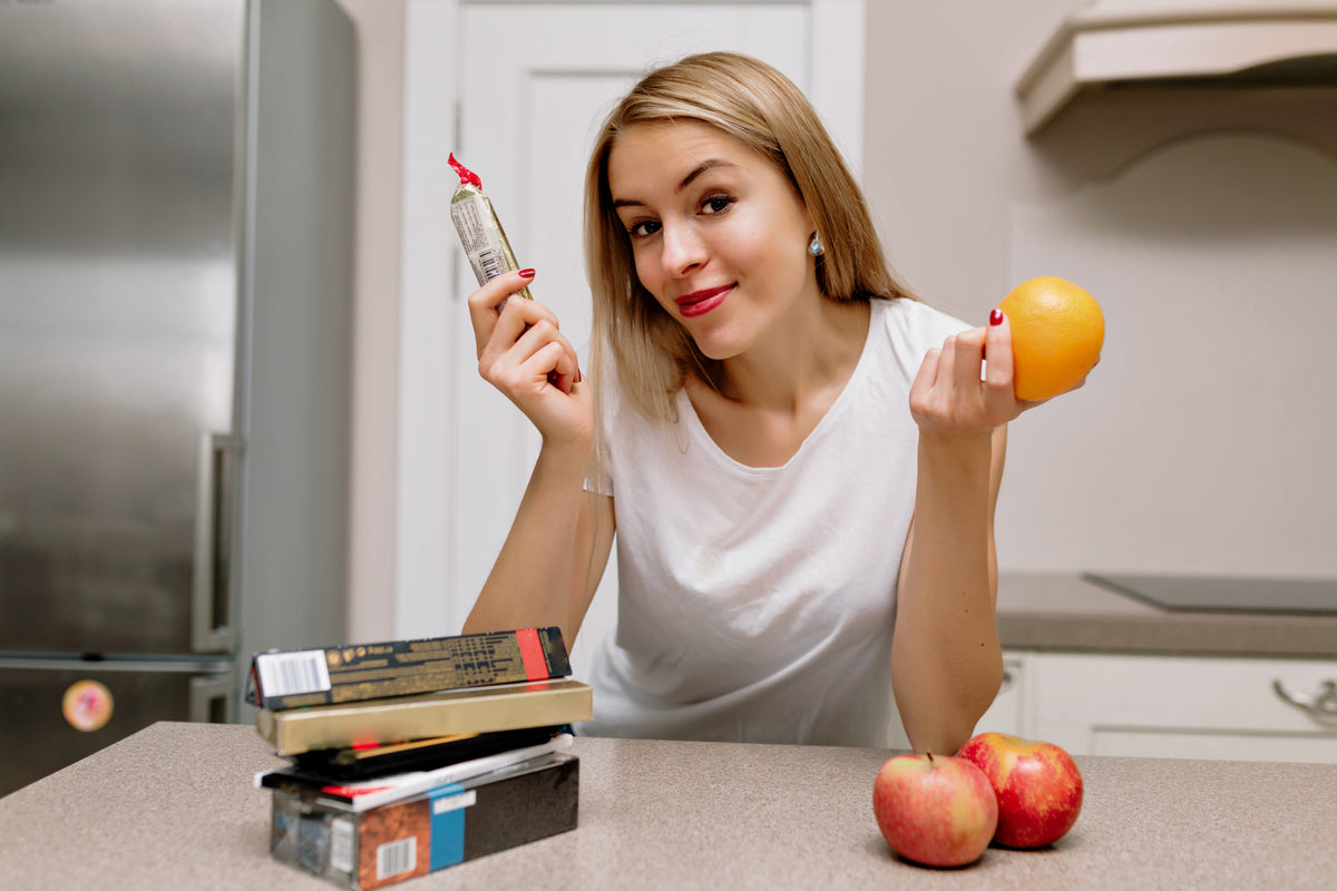 Junge Frau hält eine Orange und ein Nahrungsergänzungsmittel in der Küche.