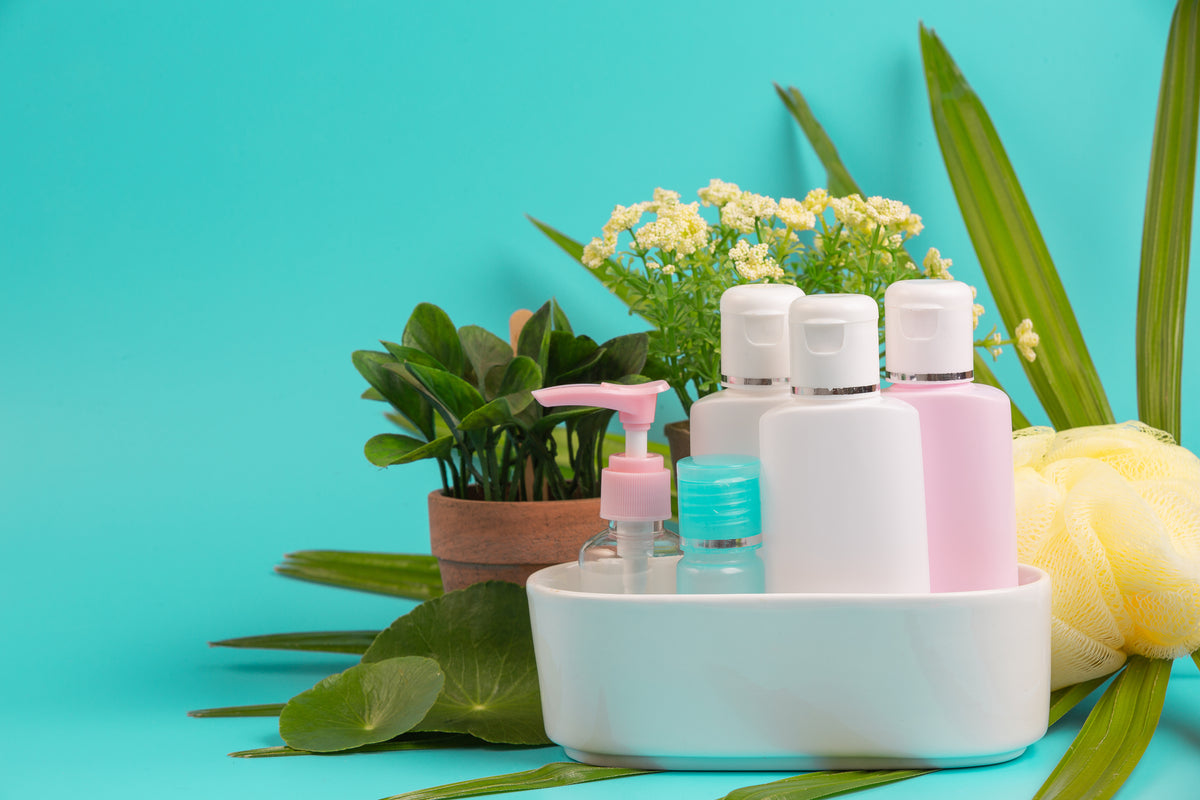 Bio-Kosmetik und Pflegeprodukte in einer Schale mit grünen Pflanzen auf türkisfarbenem Hintergrund