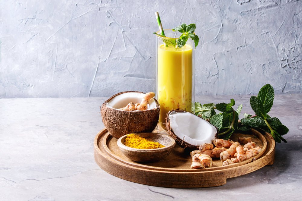 Ein köstlicher gelber kurkuma kokos smoothie in einem klaren glas mit frischer minz garnitur entdecke köstliche gärgetränke