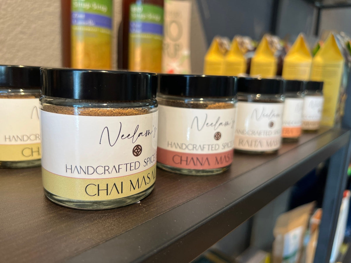 Ein klares glassglas mit schwarzem deckel und weißem etiket, das neelams handgefertigte chai masala gewürze im mana shop zeigt