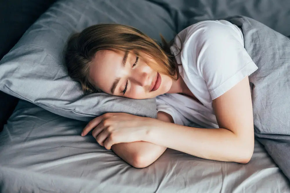 Eine frau schläft entspannt auf einem bett mit grauem kissen und weißem t-shirt als entspannung mittel