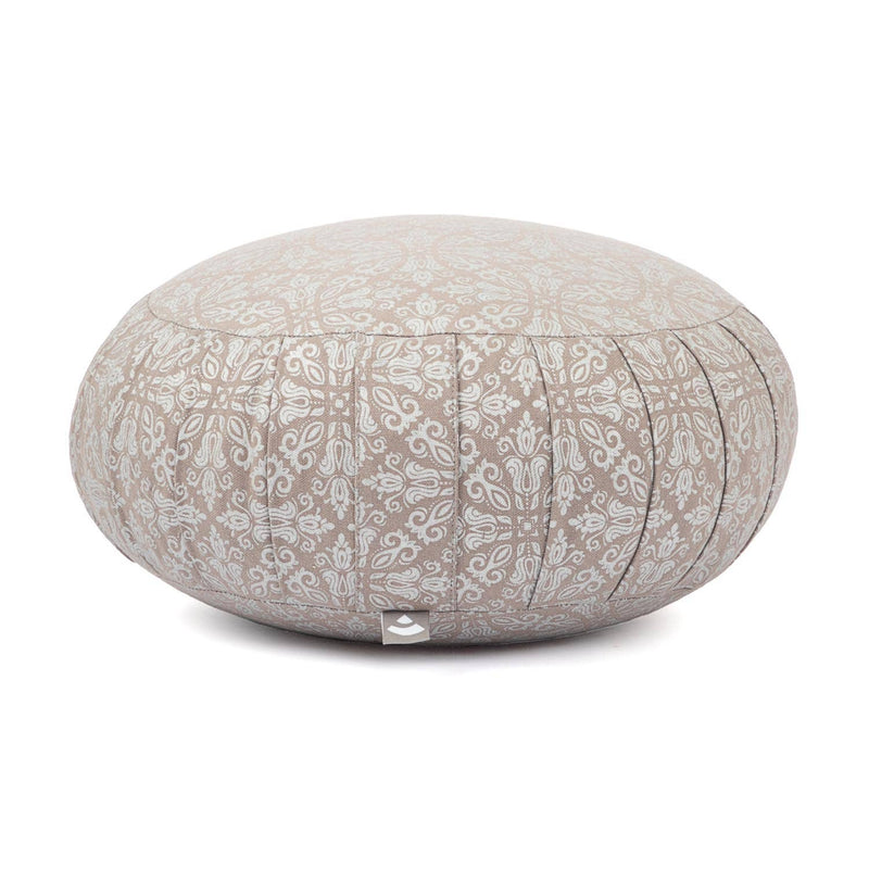 Ein runder Meditationskissen in hellem Beige mit einem weißen dekorativen Muster, von der Seite gezeigt. Das Kissen hat ein kleines Etikett an der Unterseite, und sein Design wird vor einem weißen Hintergrund hervorgehoben