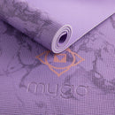 Eine Makro-Nahaufnahme einer lila Yogamatte mit Marmormuster, die das geprägte „myga“-Logo und die feine Textur der rutschfesten Oberfläche zeigt.