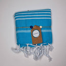 Ein gefaltetes blau gestreiftes Handtuch mit weißen Fransen, einem braunen Etikett und Perlen.