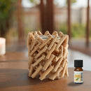 Eine Flasche des ätherischen Öls Zen'Arôme Tea Tree steht neben einem rustikalen Kerzenhalter, der aus ineinander verflochtenen, hellen Holzstäbchen gefertigt ist.