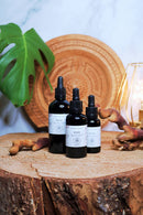 Drei dunkle Glasflaschen mit Reishi-Flüssigextrakt auf einem Holzstamm neben einem grünen Blatt.