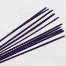 Eine Nahaufnahme eines Bündels dunkelvioletter Räucherstäbchen, die verstreut auf einer weißen Oberfläche mit Marmormuster liegen.