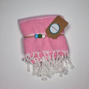 Ein gefaltetes rosa gestreiftes Handtuch mit weißen Fransen, einem braunen Etikett und bunten Perlen.