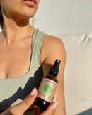 Frau in einem Top hält eine Sprühflasche PAAVANI AYURVEDA Anti-Juckreiz-Mittel in der Nähe ihrer Schulter.