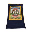 Ein rechteckiger tibetischer Thangka-Stoff mit einer zentralen Darstellung einer vierarmigen Gottheit auf einem Lotus, umrahmt von Gelb und Blau, vor einem Landschaftshintergrund mit Wolken, auf weißem Hintergrund.