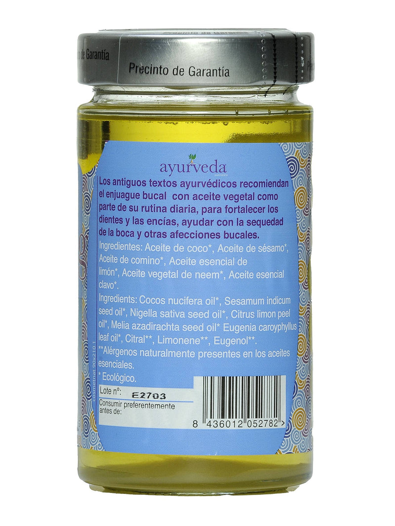 Ein gelbes Ölglas mit einem blauen Etikett, das eine Beschreibung der ayurvedischen Mundspülung sowie die Inhaltsstoffe, Allergene und die Chargennummer E2703 auflistet.