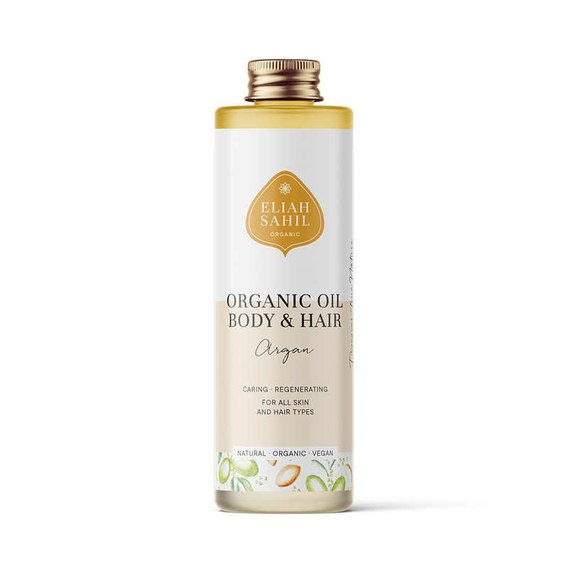 Produktfoto einer hohen weißen Flasche „Eliah Sahil Organic Oil Body & Hair Argan“ mit einem hellbraunen Etikett und goldenem Logo, das besagt, dass es pflegend und regenerierend für alle Haut- und Haartypen ist.