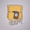 Ein gefaltetes gelb gestreiftes Handtuch mit einem braunen Etikett und bunten Perlen.