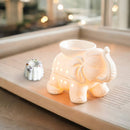 Beleuchtete weiße Keramik-Duftlampe in Elefantenform neben einem Wachsmelt auf einem Holztablett.