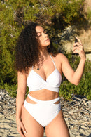 Frau in einem weißen Bikini-Oberteil sprüht sich ein Produkt auf Gesicht oder Hals im Freien.