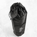 Eine aufrecht stehende schwarze, zylindrische Yogamatten-Tasche mit Kordelzug und dem vertikalen weißen „myga“-Logo ist auf einer hellgrauen, strukturierten, marmorartigen Oberfläche abgebildet.