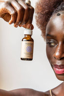 Eine dunkelhäutige Frau hält eine Flasche Paavani Ayurveda Tridoshic Serum für ausgeglichene Haut neben ihr Gesicht.