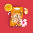 Eine Packung Chakras Ayurvedische Infusion: Hibiskus & Orange Tee liegt auf einem roten Hintergrund, umgeben von einer halbierten Orange, Orangenschale und rosa Hibiskusblüten.